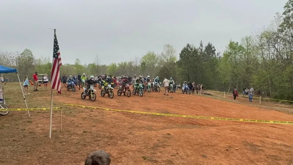 A long row of mini bikes lined up at the start behind the American flag, with parents alongside