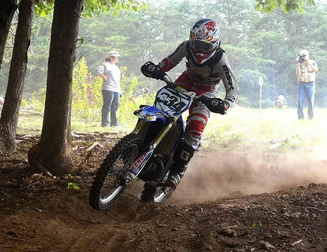 Dakota racing #334 in the woods, front wheel up out of a rutted corner in a cloud of dust